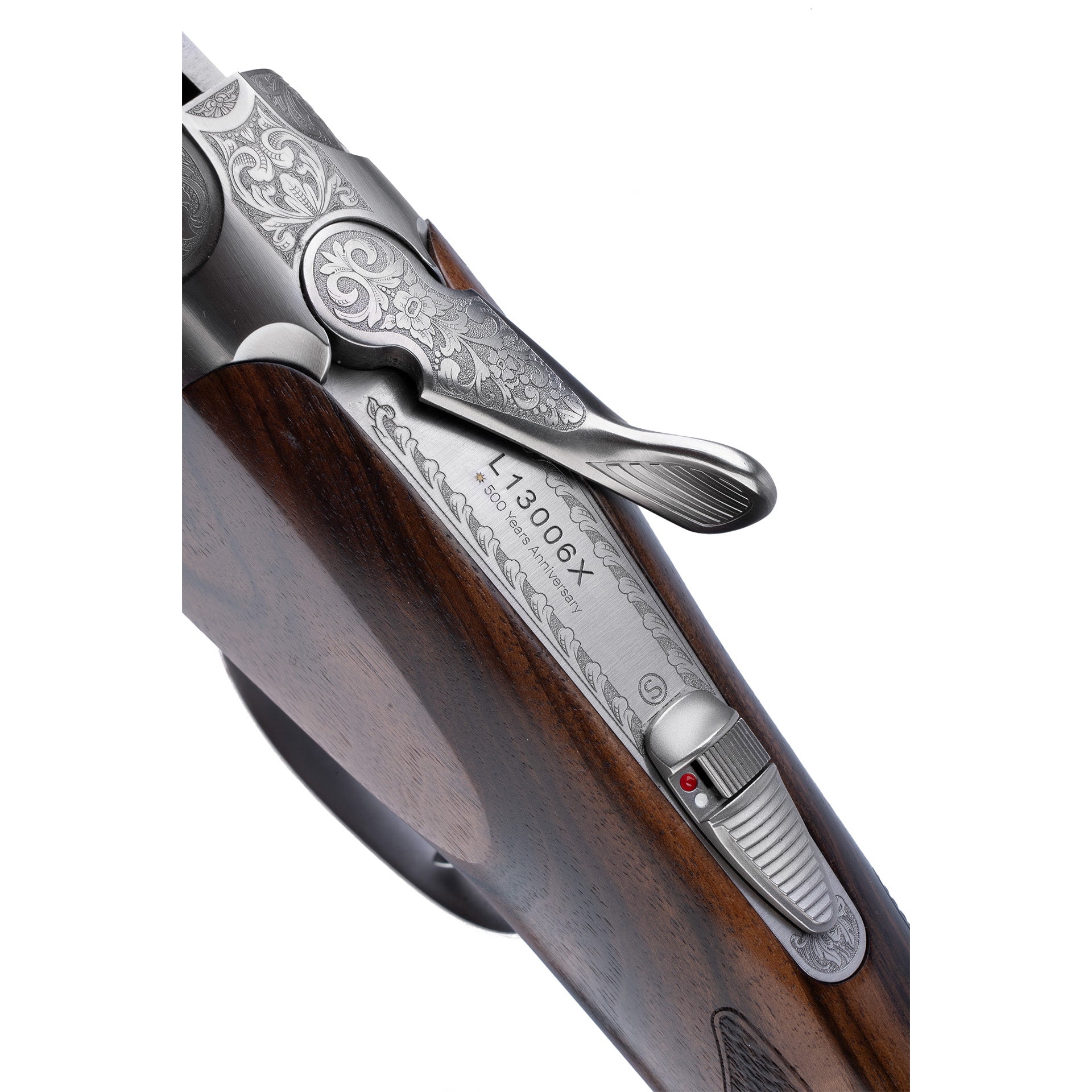 Close-up of a shotgun receiver and leveret with ornate silver engraving and a dark brown wooden stock on a white background.