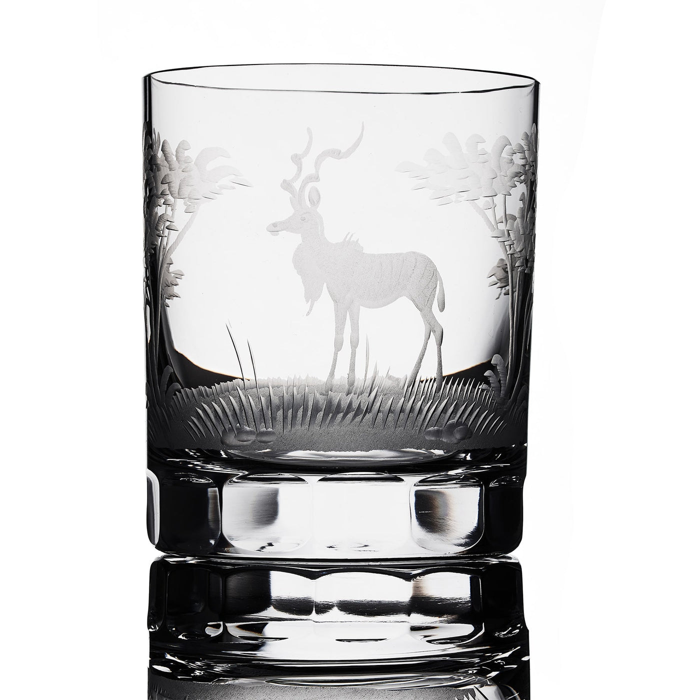 A clear crystal glass with a hand-engraved image of a kudu antelope in a grassy landscape.