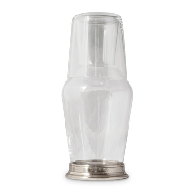 A clear glass bedside carafe with a matching tumbler, featuring a pewter band on the carafe and a glass lid on the tumbler.