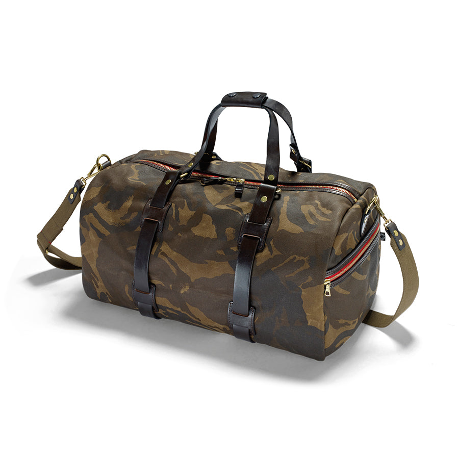 A camouflage patterned duffle holdall with leather handles and a removable shoulder sling, featuring two zipped end pockets.