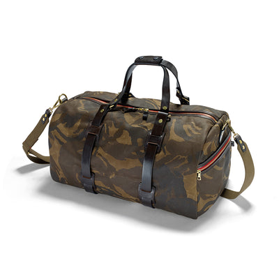 A camouflage patterned duffle holdall with leather handles and a removable shoulder sling, featuring two zipped end pockets.