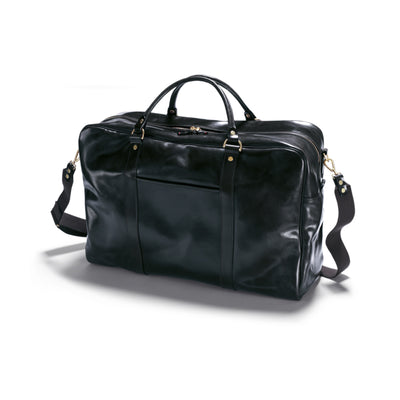 A dark Havana black leather hold all with rolled handles and a wide shoulder sling. The bag has brass feet on the base and appears to have multiple storage compartments.